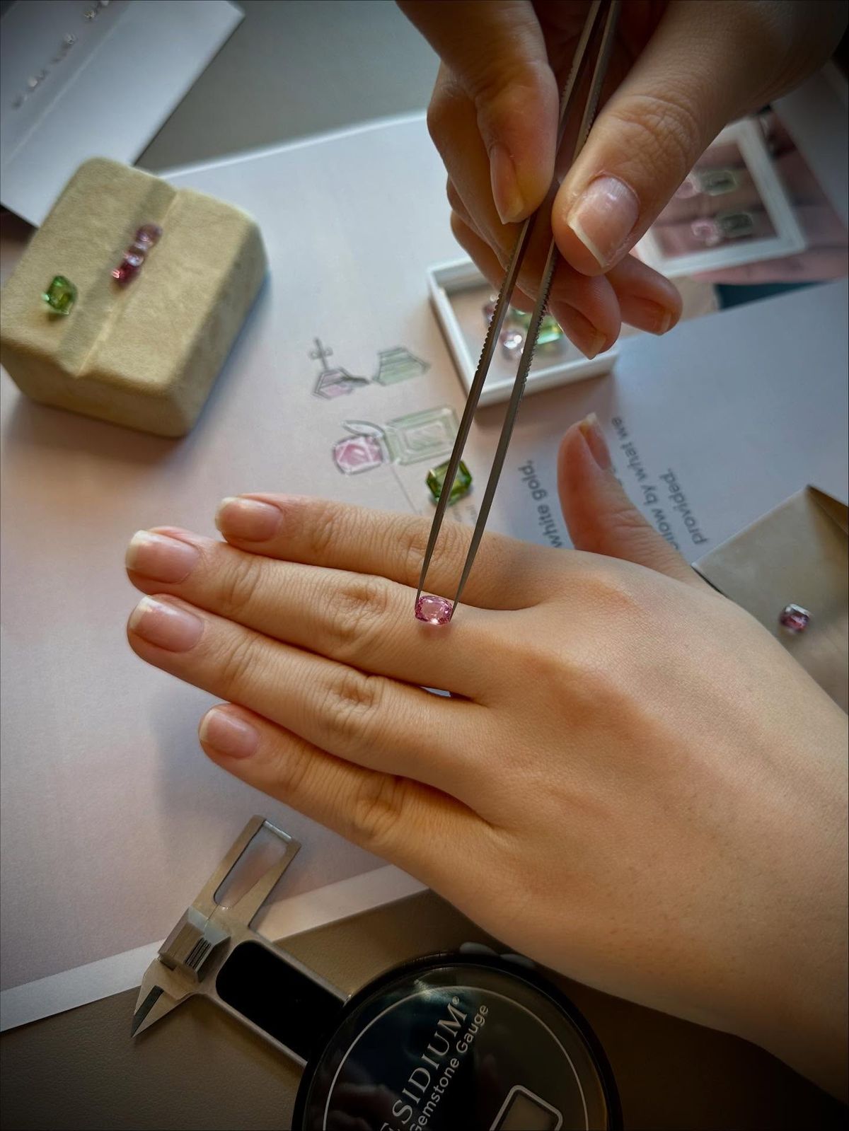 A jeweler reviewing a pink colored gemstone during the design process